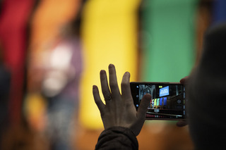 A protester photographs a speaker as she shares her story at the microphone.